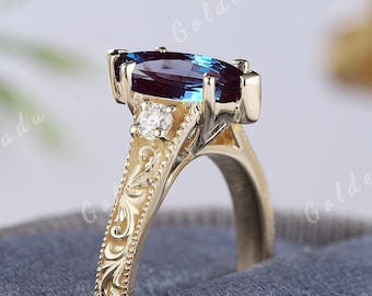Op de afbeelding: Een gouden ring met een blauwe, marquise-vormige edelsteen en twee kleinere ronde diamanten. De ring heeft een ingewikkeld bloemmotief op de band.