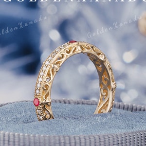 May include: A gold filigree ring with red gemstones set in the band. The ring is displayed in a blue velvet box.