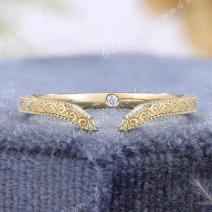 May include: A gold-colored ring with an open design. The ring features a small, clear gemstone and intricate scrollwork along the band. The text "GOLDENXANADU" is at the top of the image.
