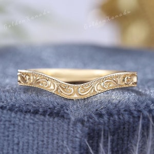 May include: A gold ring featuring an ornate, swirling filigree pattern. The ring has a curved design, with the text "GOLDENXANADU" in the background. The ring is displayed against a blue backdrop.