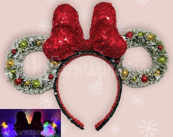 May include: Red sequined Minnie Mouse ears with a red bow and a green and white wreath on each ear. The headband is black.