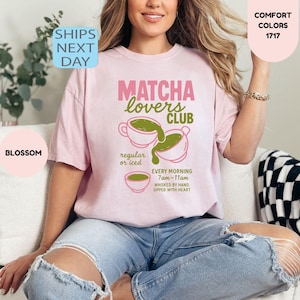 May include: A light pink t-shirt with the text "MATCHA lovers CLUB" in pink and green. The shirt features matcha tea cup illustrations and the text "regular or iced" and "EVERY MORNING 7am-11am". The shirt is part of the "COMFORT COLORS" collection.