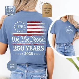 Pu&ograve; includere: Una maglietta blu jeans con un design a bandiera americana invecchiata, la scritta "We The People" e "250 YEARS 2026". La maglietta presenta anche l'anno "1776" stampato sul davanti e sul retro. Comfort Colors 1717.