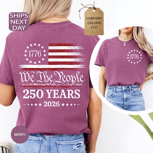 Pu&ograve; includere: T-shirt color bacca con un design a bandiera americana invecchiata. La maglietta presenta il testo "1776" e "We The People 250 YEARS 2026". Ha un girocollo e maniche corte. L'etichetta recita "Comfort Colors 1717".