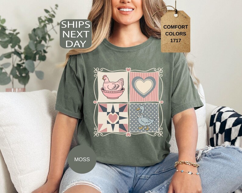 May include: A moss green t-shirt with a patchwork design featuring a hen, heart, and duck. The shirt has the text "SHIPS NEXT DAY" and a tag that says "COMFORT COLORS 1717".