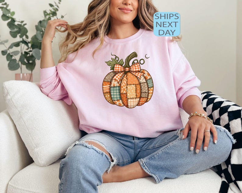 May include: A light pink sweatshirt featuring a patchwork pumpkin design with a green stem and bow. The pumpkin is made of various fabric patterns in orange, green, and brown. The text "SHIPS NEXT DAY" is in a blue box.