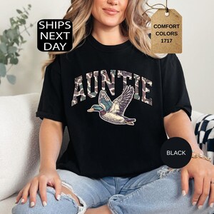 May include: Black t-shirt with the word "AUNTIE" in camouflage print and a graphic of a flying duck. The shirt also has the words "Comfort Colors 1717" on a tag.
