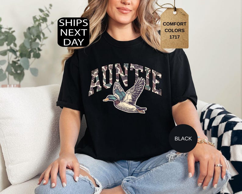 May include: Black t-shirt with the word "AUNTIE" in camouflage print and a graphic of a flying duck. The shirt also has the words "Comfort Colors 1717" on a tag.