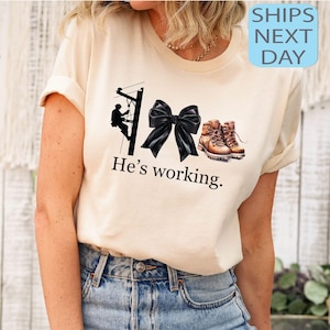 Camiseta &quot;Ele está trabalhando&quot;, camiseta de eletricista, presente para esposa de eletricista, camiseta engraçada de eletricista, moletom com laço coquete, camiseta de esposa de colarinho azul