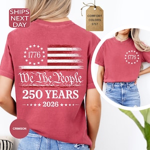 Pu&ograve; includere: T-shirt color cremisi con un design patriottico. Il design include il testo "1776", "We The People", "250 YEARS" e "2026", insieme a una bandiera americana stilizzata. Le t-shirt sono disponibili in colori comfort.