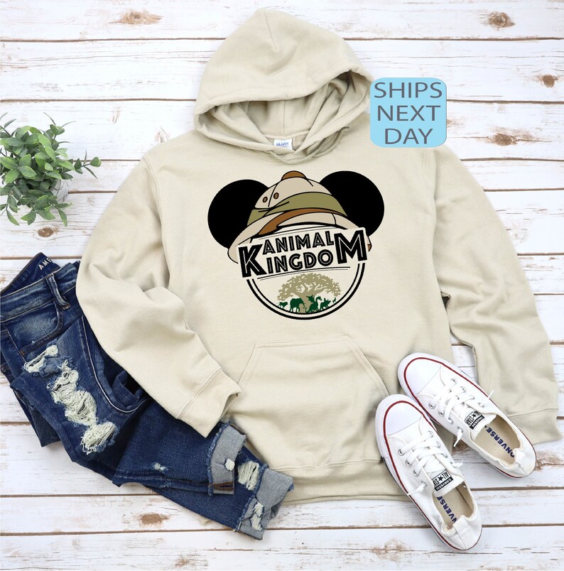 May include: A beige hoodie with a Mickey Mouse ear design featuring a safari hat and the words "Animal Kingdom" in a green circle.