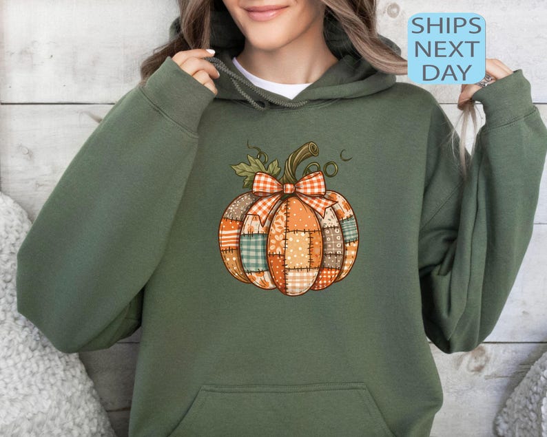 May include: An olive green hoodie featuring a patchwork pumpkin design with a plaid bow. The pumpkin has orange, brown, and green patches. The text "SHIPS NEXT DAY" is in a blue box.