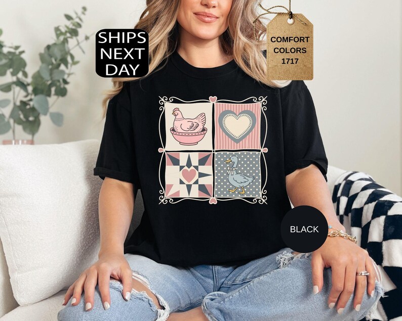 May include: Black t-shirt with a four-panel design: a hen in a bowl, a heart, a quilt pattern, and a goose. The shirt has the text "Comfort Colors 1717" on a tag and "Ships Next Day" on a black square.
