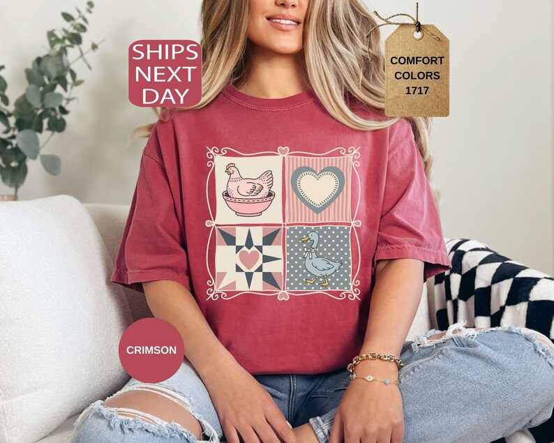 May include: Crimson t-shirt with a patchwork design featuring a hen, heart, and goose. The shirt has the text "SHIPS NEXT DAY" and "COMFORT COLORS 1717" on a tag. The shirt is a relaxed fit.