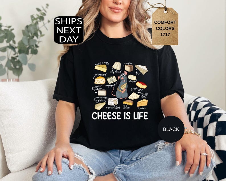 May include: Black t-shirt with a graphic of various cheeses and a cartoon rat holding a cheese wedge. The text "CHEESE IS LIFE" is below the graphic. The shirt also has the text "SHIPS NEXT DAY" and "COMFORT COLORS 1717".