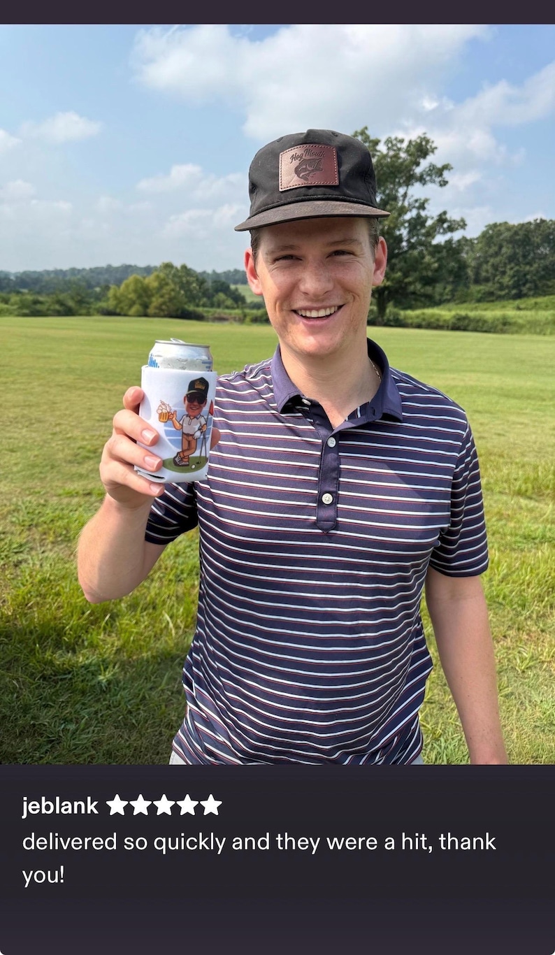 May include: A white foam beverage insulator featuring a graphic of a cartoon golfer holding a beer and a golf club. The insulator is held up, displaying the colourful illustration against a dark blue, white, and red striped polo shirt.
