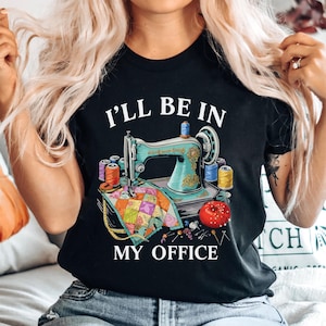 A woman wearing a black t-shirt with a graphic design of a sewing machine surrounded by sewing supplies, along with the text "I'll be in my office".