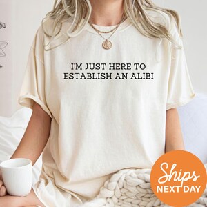 A person wearing a white t-shirt with the text "I'M JUST HERE TO ESTABLISH AN ALIBI" printed on it.