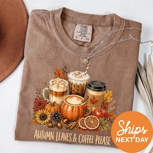 A t-shirt with a graphic design depicting autumn leaves and coffee, along with a necklace and a hat, all set against a white background.
