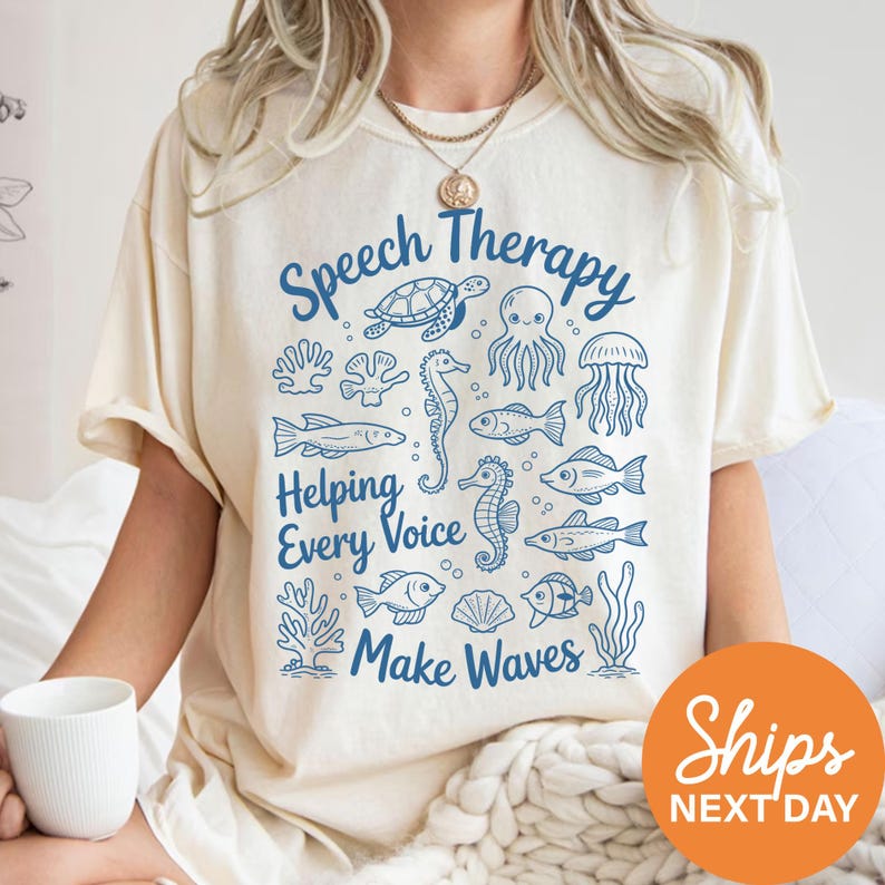 A person wearing a white t-shirt with a graphic design featuring various sea creatures and the text "Speech Therapy Helping Every Voice Make Waves" printed on it.
