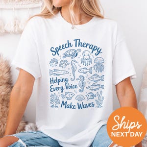 A woman wearing a white t-shirt with a graphic design featuring various sea creatures and the text "Speech Therapy Helping Every Voice Make Waves".