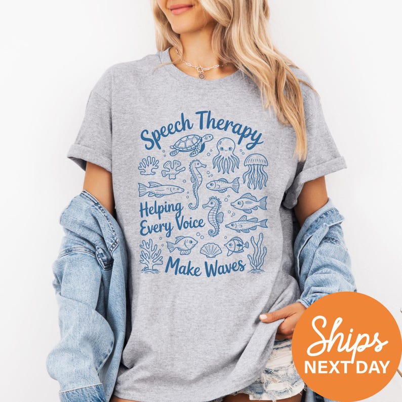 A woman wearing a gray t-shirt with a graphic design of marine life and text that says "Speech Therapy Helping Every Voice Make Waves".