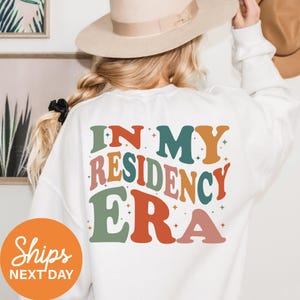 a woman wearing a white shirt that says i'm my residence era