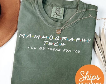 Peut inclure: Un t-shirt vert olive à col rond avec une étiquette Comfort Colors. Le t-shirt présente un texte blanc indiquant MAMMOGRAPHY TECH avec des points colorés entre les lettres et la phrase I'LL BE THERE FOR YOU imprimée en dessous en blanc.