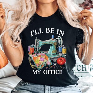 A woman wearing a black t-shirt with a graphic design of a sewing machine surrounded by sewing supplies, along with the text "I'll be in my office".