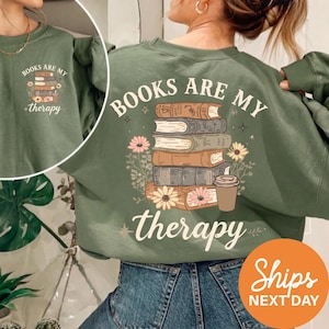A woman wearing a green sweatshirt with the text "BOOKS ARE MY THERAPY" printed on it, along with an illustration of a stack of books and flowers.