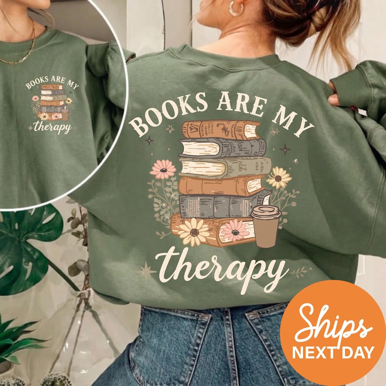 A woman wearing a green sweatshirt with the text "BOOKS ARE MY THERAPY" printed on it, along with an illustration of a stack of books and flowers.