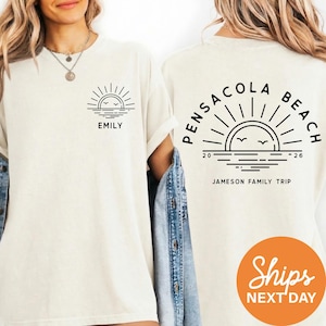 two white t-shirts with black text and graphics. The t-shirt on the left has the text "EMILY" and the t-shirt on the right has the text "PENSCOLA BEACH" and "JAMESON FAMILY TRIP". There is also a small orange circle with the text "ShIPS NEXT DAY" in the bottom right corner.