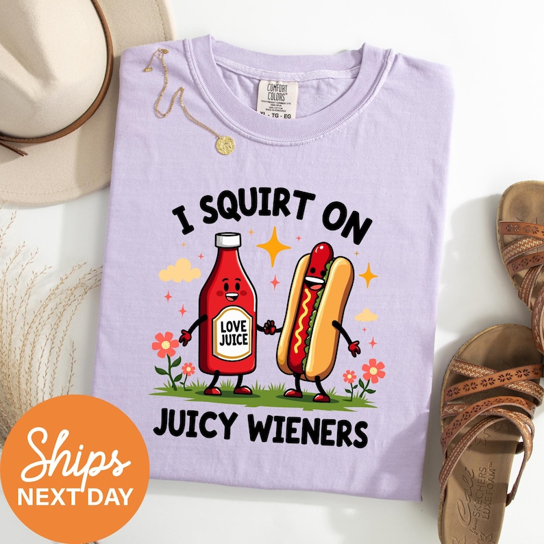 a purple t-shirt with a cartoon hot dog and a ketchup bottle, along with a pair of sandals and a hat, all arranged on a white surface.