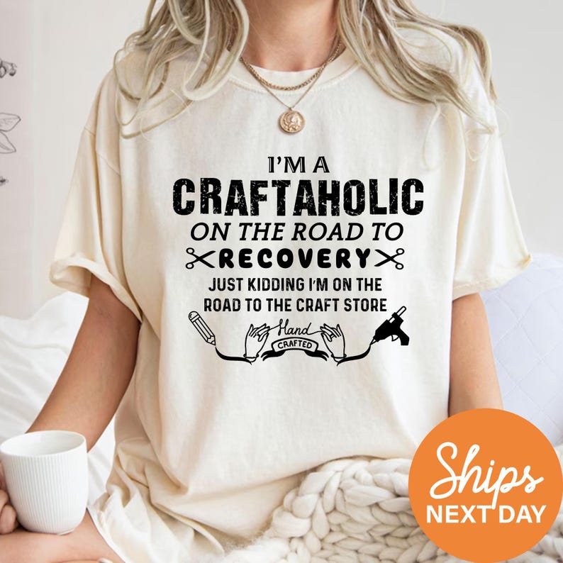 A person wearing a white t-shirt with a humorous text printed on it, sitting on a bed with a cup of coffee.
