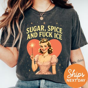 A woman wearing a black t-shirt with a graphic design featuring a woman holding a wand and a heart-shaped background with stars.