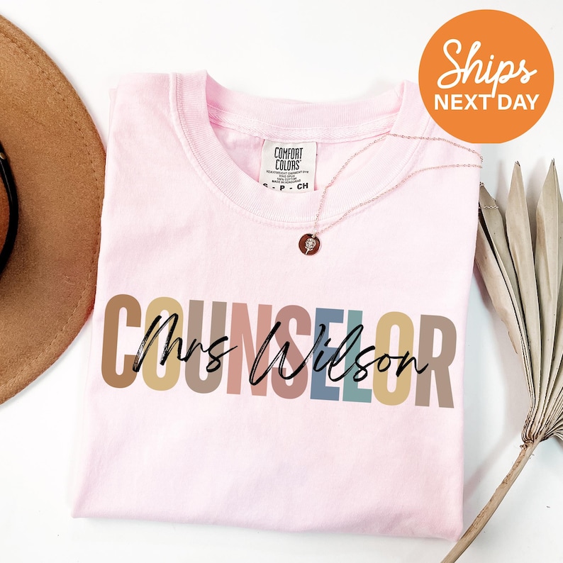 a pink shirt with the word's name on it next to a hat and