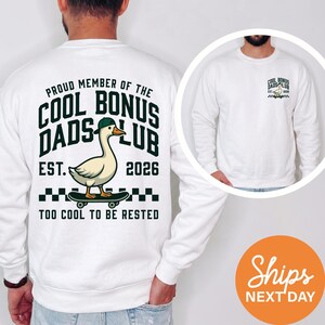 May include: White sweatshirt with a graphic that reads "Proud Member of the Cool Bonus Dads Club" with a duck on a skateboard. The design includes the text "Est. 2026" and "Too Cool to Be Rested."