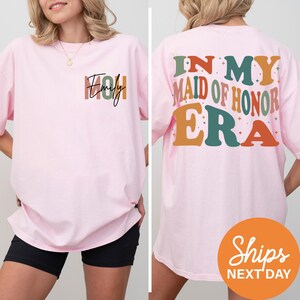 a woman wearing a pink shirt that says i'm my maid of honor era