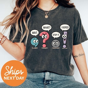 May include: Dark gray t-shirt featuring cartoon punctuation marks with speech bubbles saying "WAIT," "WHAT?," "STOP IT," and "I AGREE!" The shirt has a relaxed fit and a vintage wash.