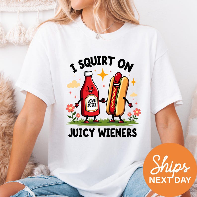 A white t-shirt with a graphic design featuring a hot dog and a ketchup bottle, along with the text "I SQUIRT ON JUICY WIENERS" and a "Ships NEXT DAY" logo.