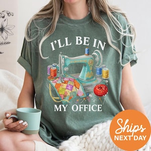 A woman wearing a green t-shirt with a sewing machine and sewing supplies printed on it, holding a cup of coffee.