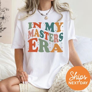 a woman sitting on a bed wearing a t - shirt that says in my masters