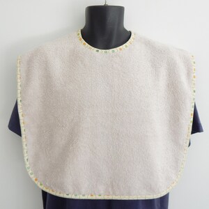 May include: A beige baby bib with a colourful trim around the edges. The bib is made of a soft, absorbent material.