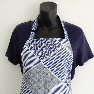 May include: A blue and white patterned apron with a geometric design. The apron has adjustable straps and a neck strap.