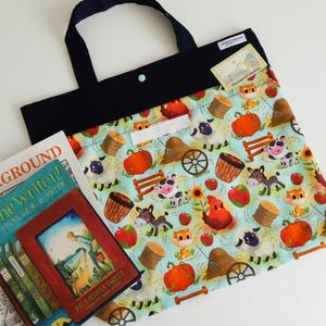 May include: A blue tote bag with a black top and handles, decorated with a farmyard pattern of pumpkins, animals, and hay bales. A book with a red frame is visible.
