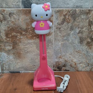 May include: Pink Hello Kitty electric milk frother with a white Hello Kitty character on top. The frother has a cord and a base with a Hello Kitty logo.