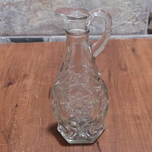 May include: A clear glass bottle with a textured surface and a handle. The bottle has a star-shaped design.