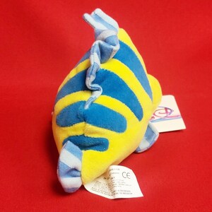 K&ouml;nnte beinhalten: Ein Pl&uuml;schtierfisch mit gelben und blauen Streifen und einer blau-wei&szlig; gestreiften Flosse. Das Spielzeug hat ein angebrachtes Etikett. Der Hintergrund ist einfarbig rot.