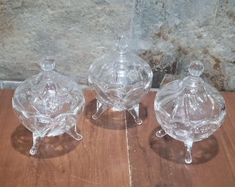 May include: Three clear glass lidded candy dishes with a decorative pattern. Each dish has three legs.