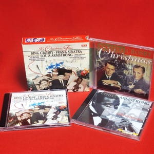 Puede incluir: Una colección de CD con temática navideña con Bing Crosby, Frank Sinatra y Louis Armstrong. Los CD están en estuches de plástico transparente y una caja de cartón, con imágenes de los artistas y decoraciones festivas. El fondo es rojo liso.
